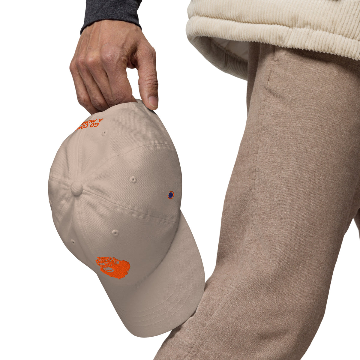 beige cap with a orange logo held by a person wearing beige pants on a white background
