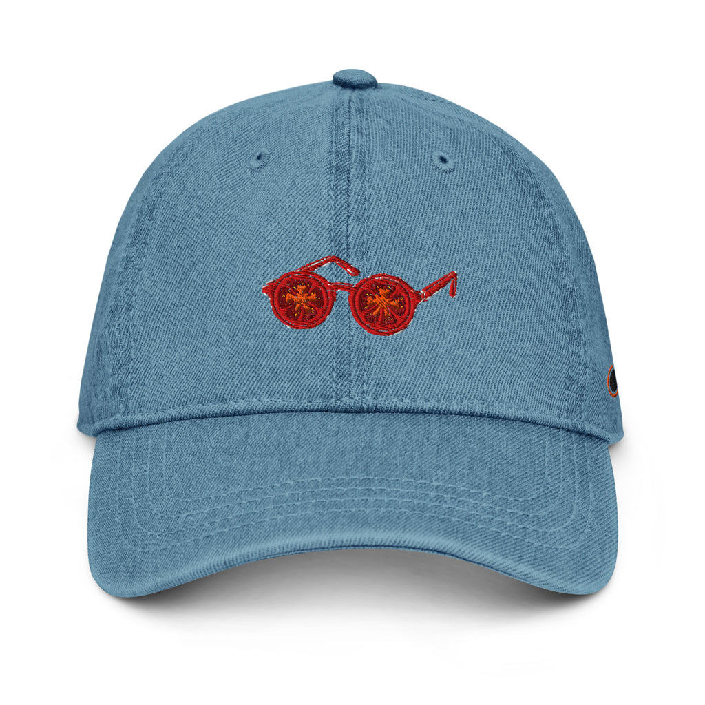 A light blue denim baseball cap featuring an embroidered pair of red sunglasses with tomato eyes on the front, set against a plain white background.
