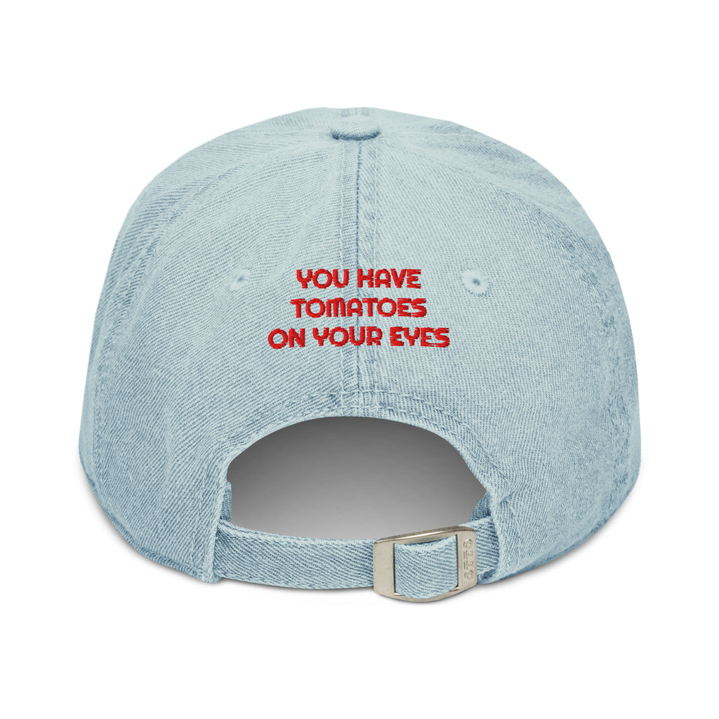 A light blue denim baseball cap shown from the back, featuring the red embroidered text 'YOU HAVE TOMATOES ON YOUR EYES' and an adjustable metal buckle.