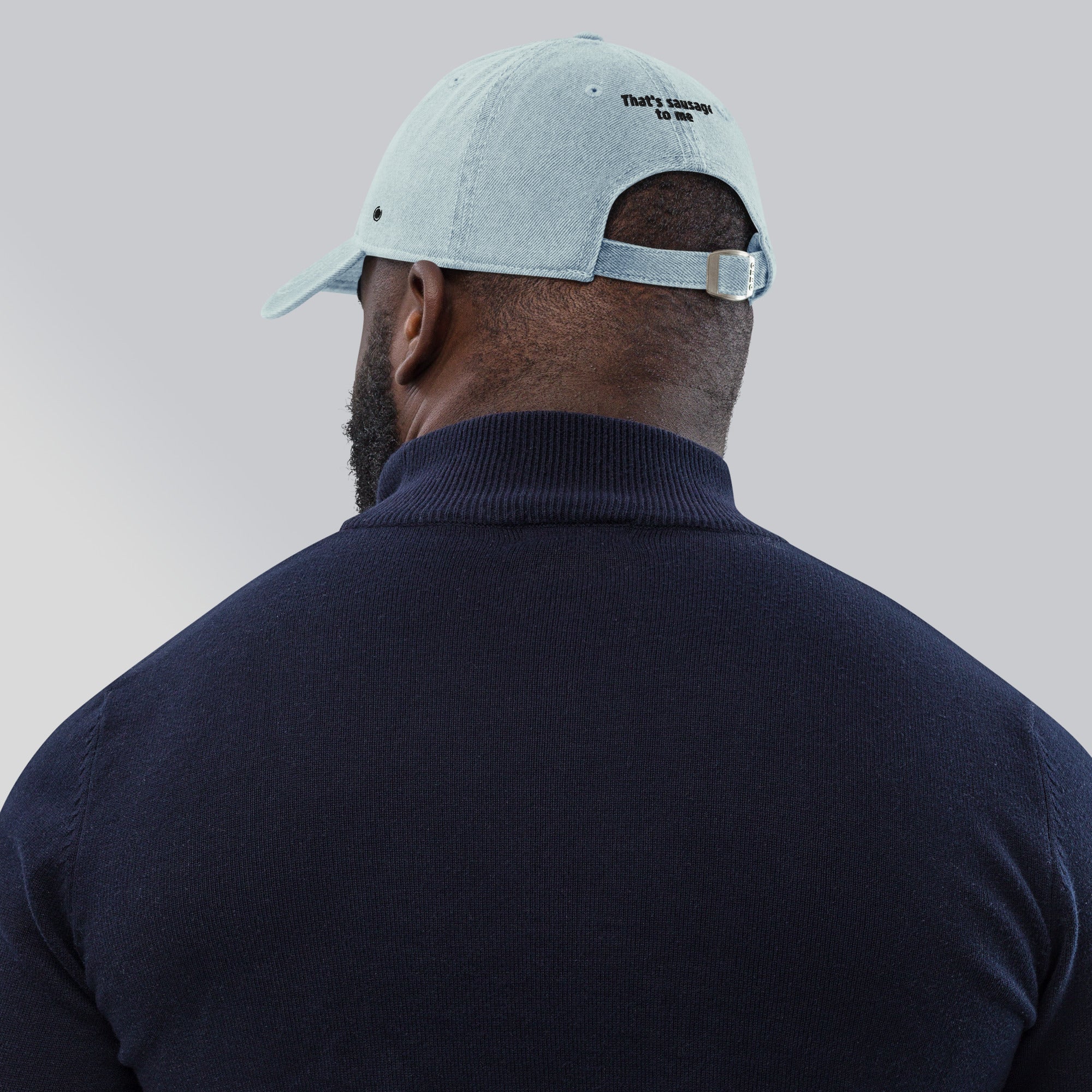 A man viewed from behind wearing a light blue baseball cap with embroidered text that says "That's sausage to me" on the back of the cap