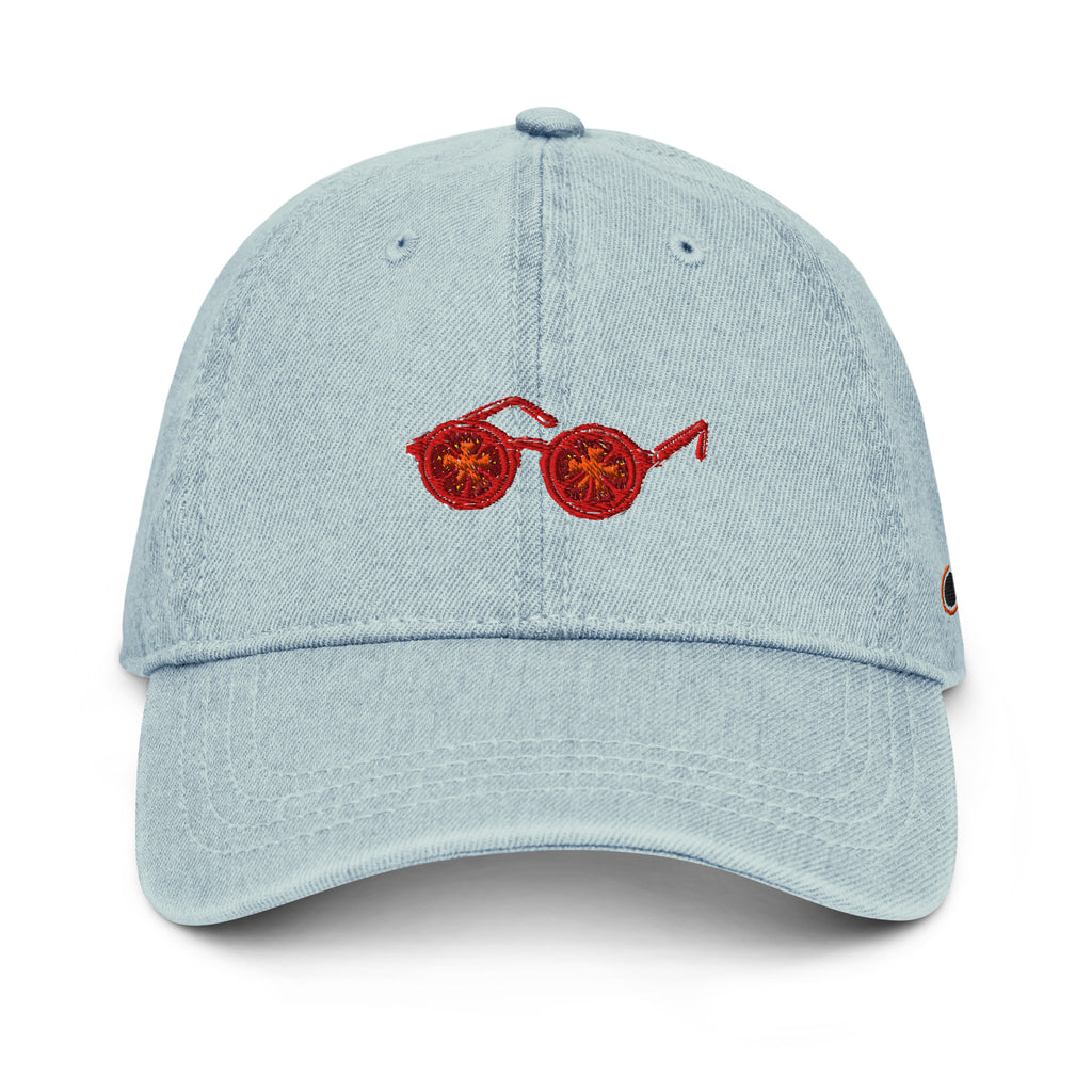 A light blue denim baseball cap featuring an embroidered pair of tomatosunglasses on the front, set against a plain white background.