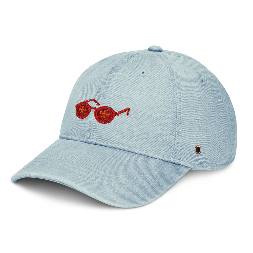 A light blue denim baseball cap featuring an embroidered red pair of sunglasses on the front panel, set against a plain white background.