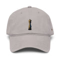 A light gray dad hat baseball cap featuring a small embroidered pepper grinder graphic on the front and a small orange embroidered logo on the side, set against a plain white background.