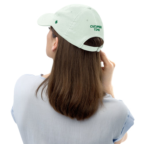 Woman wearing a light green cap with embroidered cucumber time on a white background