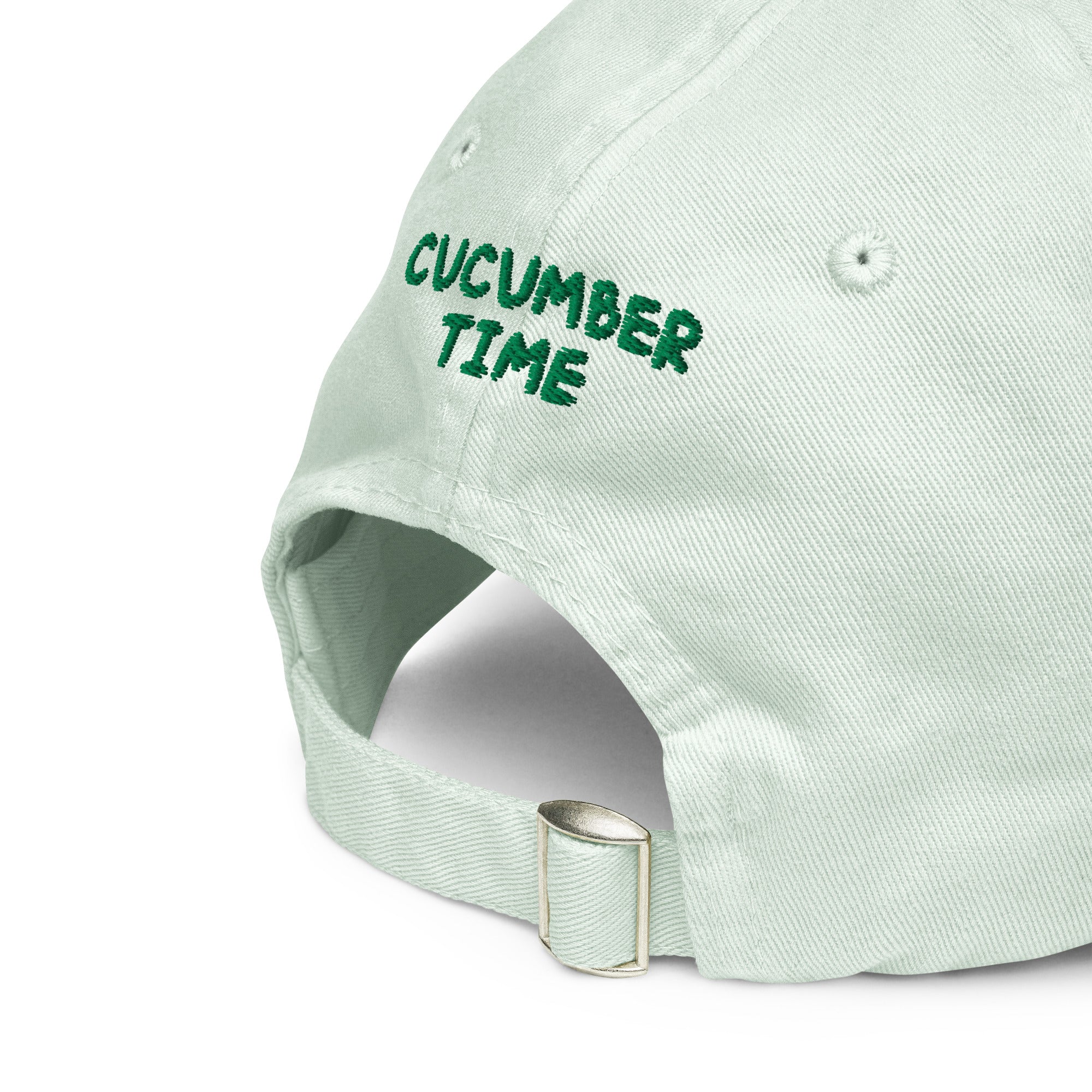 A close-up of a light mint green baseball cap with 'CUCUMBER TIME' embroidered in dark green on the side, showing the adjustable strap and metal buckle.