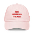 A light pink dad hat baseball cap with red embroidered text on the front that reads 'I CAN HAHA AND JAJA I'M BILINGUAL'.
