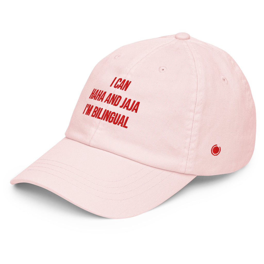 A light pink baseball cap with red embroidered text reading 'I CAN HAH AND JAJA I'M BILINGUAL' on the front, shown on a clean white background.