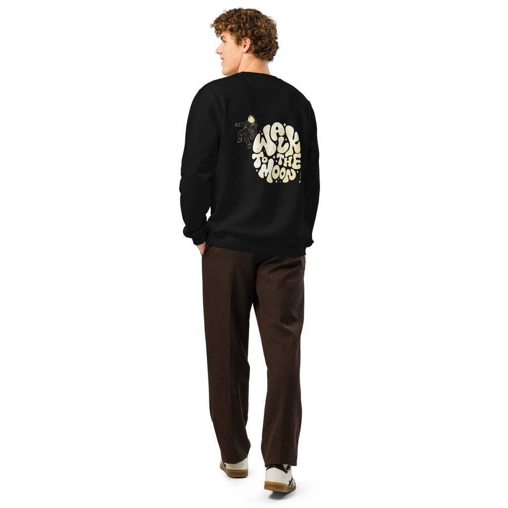A man shown from the back wearing a black crewneck sweatshirt with a large cream graphic on the back paired with brown pants and white sneakers, against a plain white background.