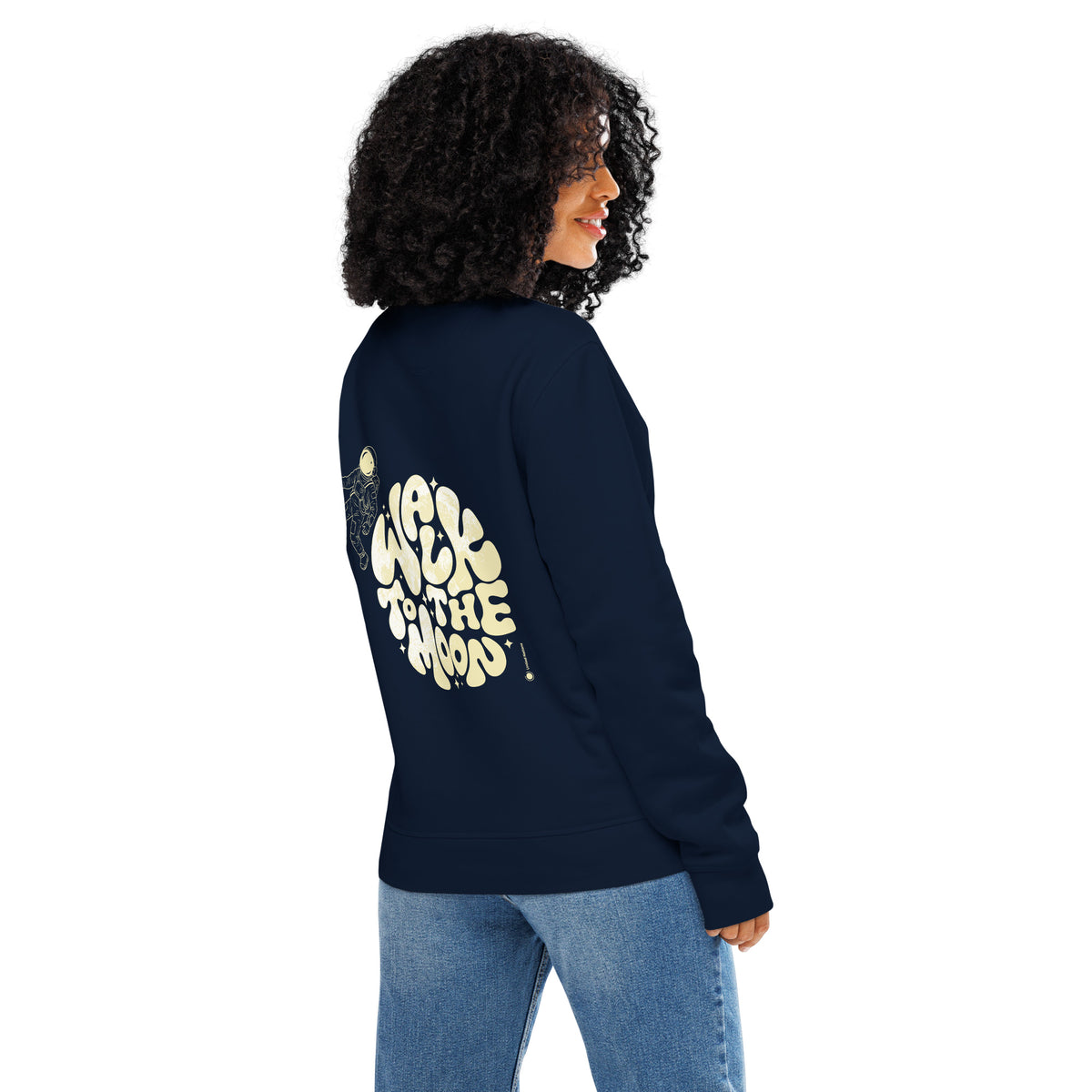 A woman with curly black hair is shown from the back wearing a navy blue sweatshirt with a large cream graphic and light blue jeans, set against a plain white background.