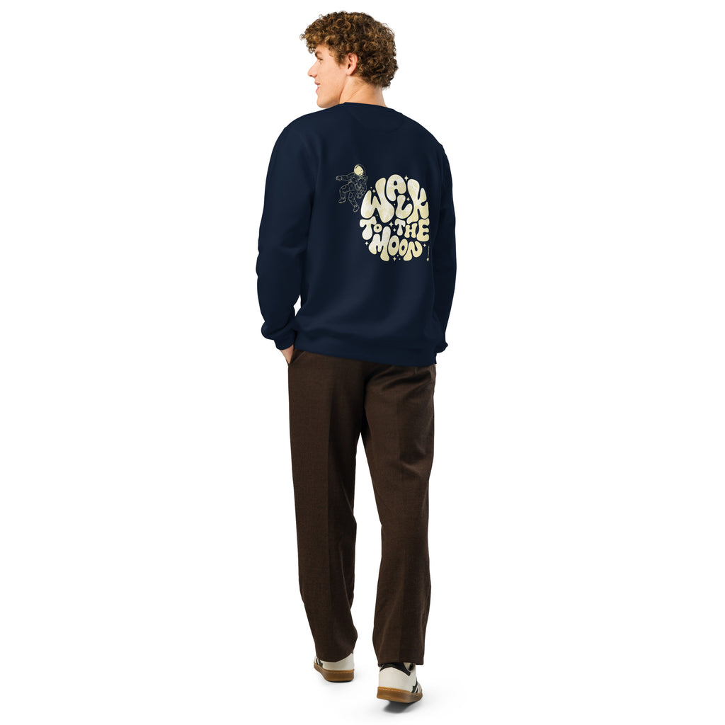 A man shown from the back wearing a navy blue crewneck sweatshirt with a large cream graphic on the back paired with brown pants and white sneakers, against a plain white background.