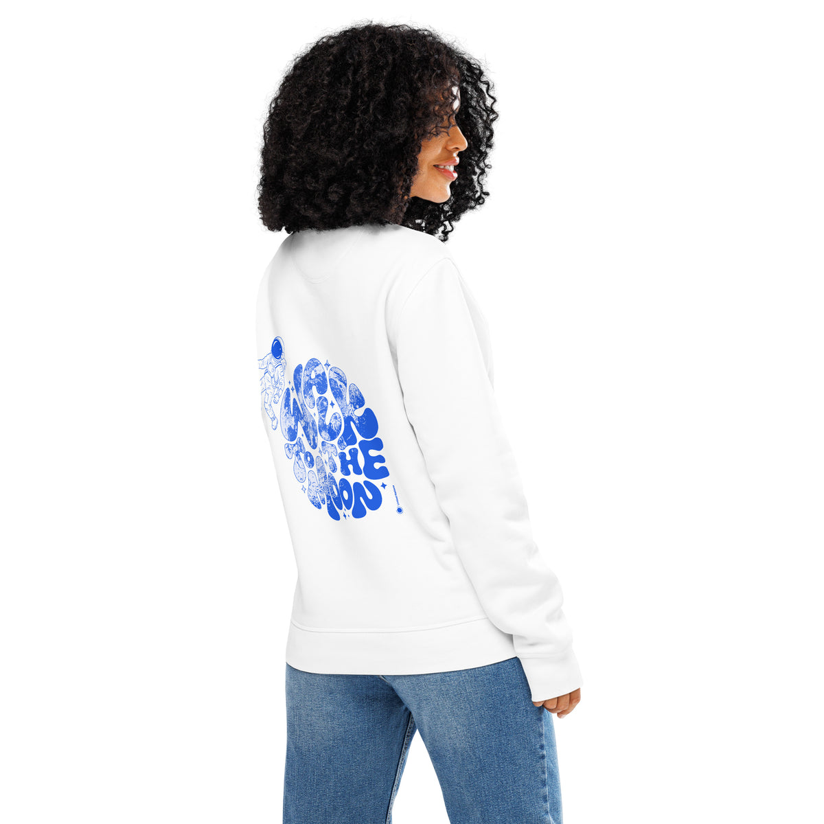 A woman with curly black hair is shown from the back wearing a white sweatshirt with a large blue graphic print on the back, paired with blue jeans, against a plain white background.