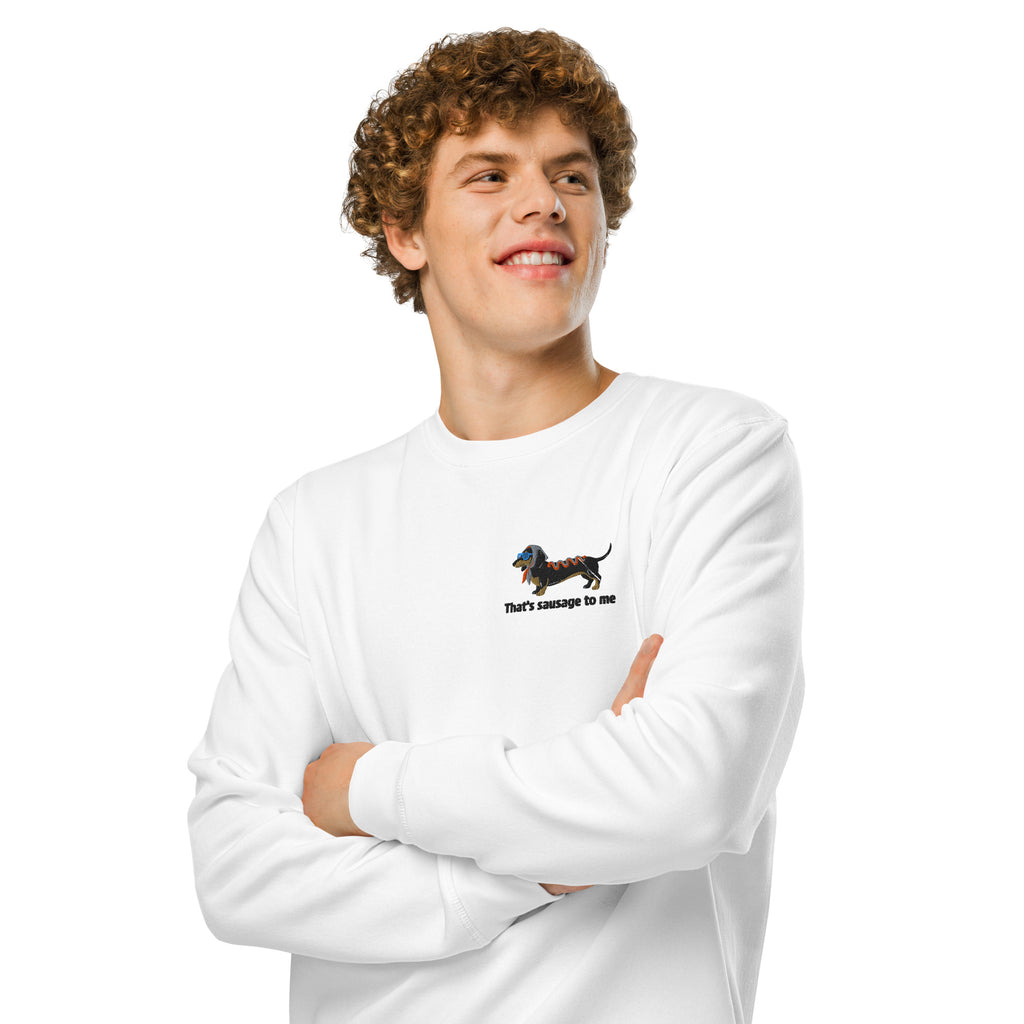 A smiling young man with curly brown hair wearing a white crewneck sweatshirt with a small dachshund graphic and the text 'that's sausage to me' on the left chest, posed with arms crossed against a solid white background.