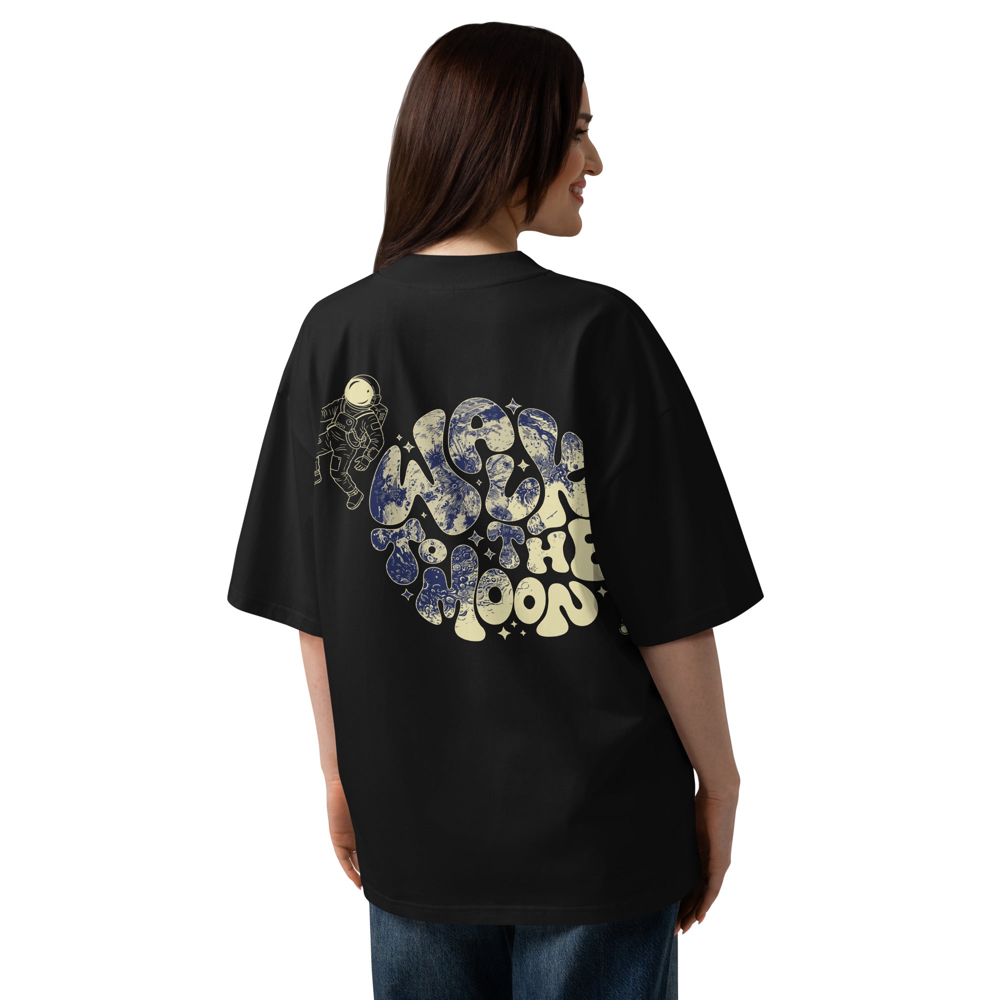 A woman shown from the back wearing an oversized black t-shirt with a large graphic print on the back. The graphic features the words 'WALK TO THE MOON' in a retro, bubbly font filled with blue and cream illustrations of planets and space-themed motifs.