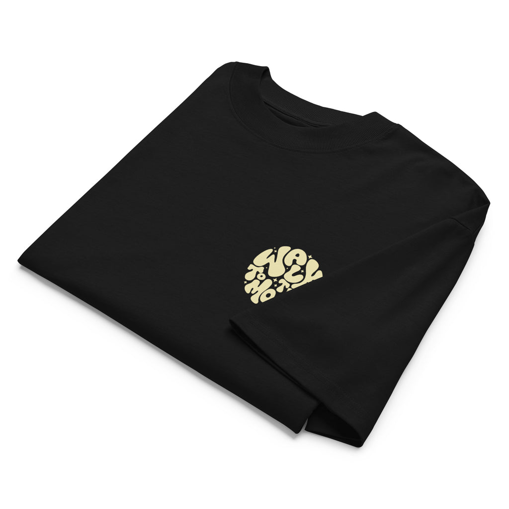 A folded black crewneck t-shirt with a small circular graphic on the left chest featuring the word 'WALK TO THE MOON' in a light beige stylized font, set against a plain white background.