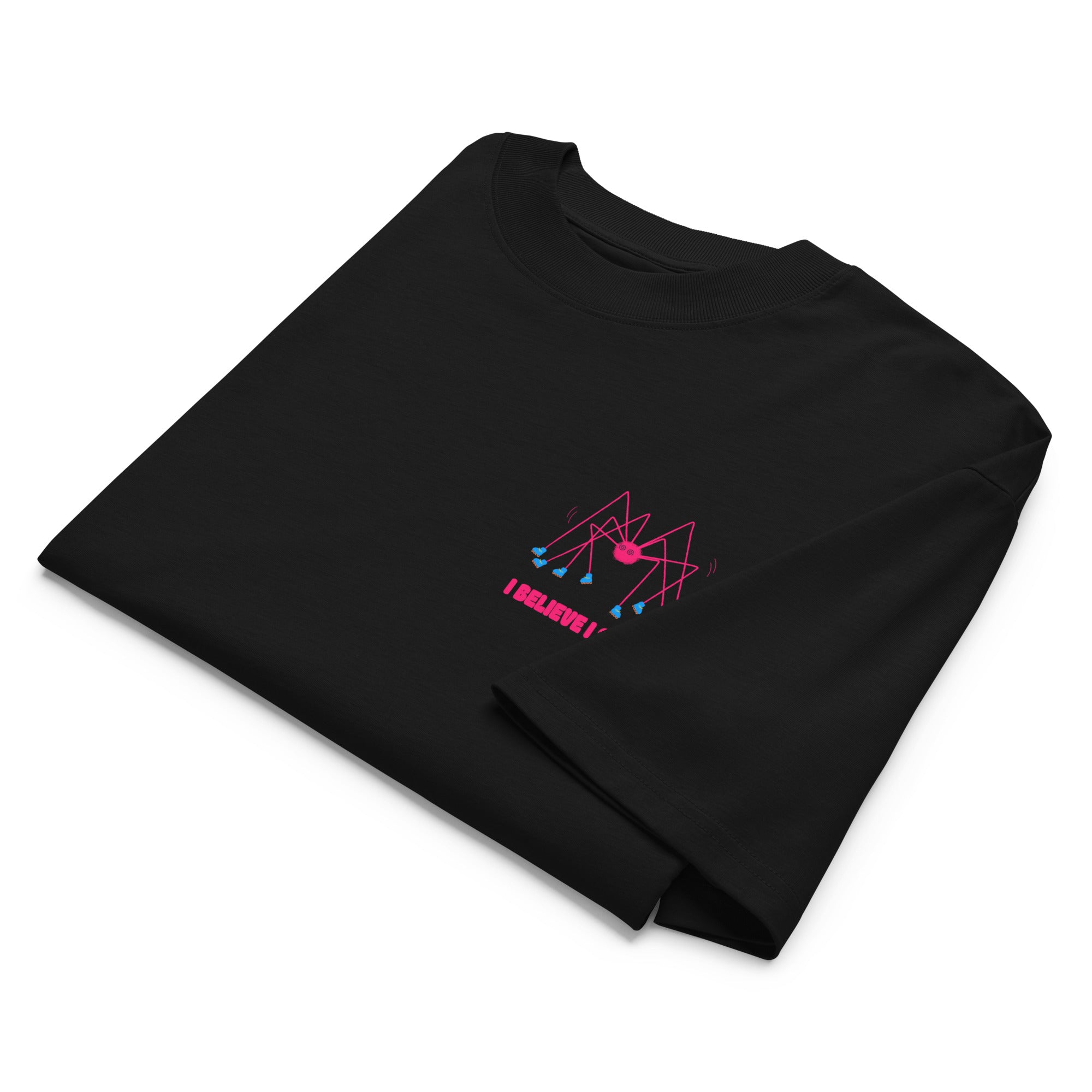 A folded black oversized graphic tshirt with a pink spider wearing roller skates and the text "I believe I spider" printed on the left chest