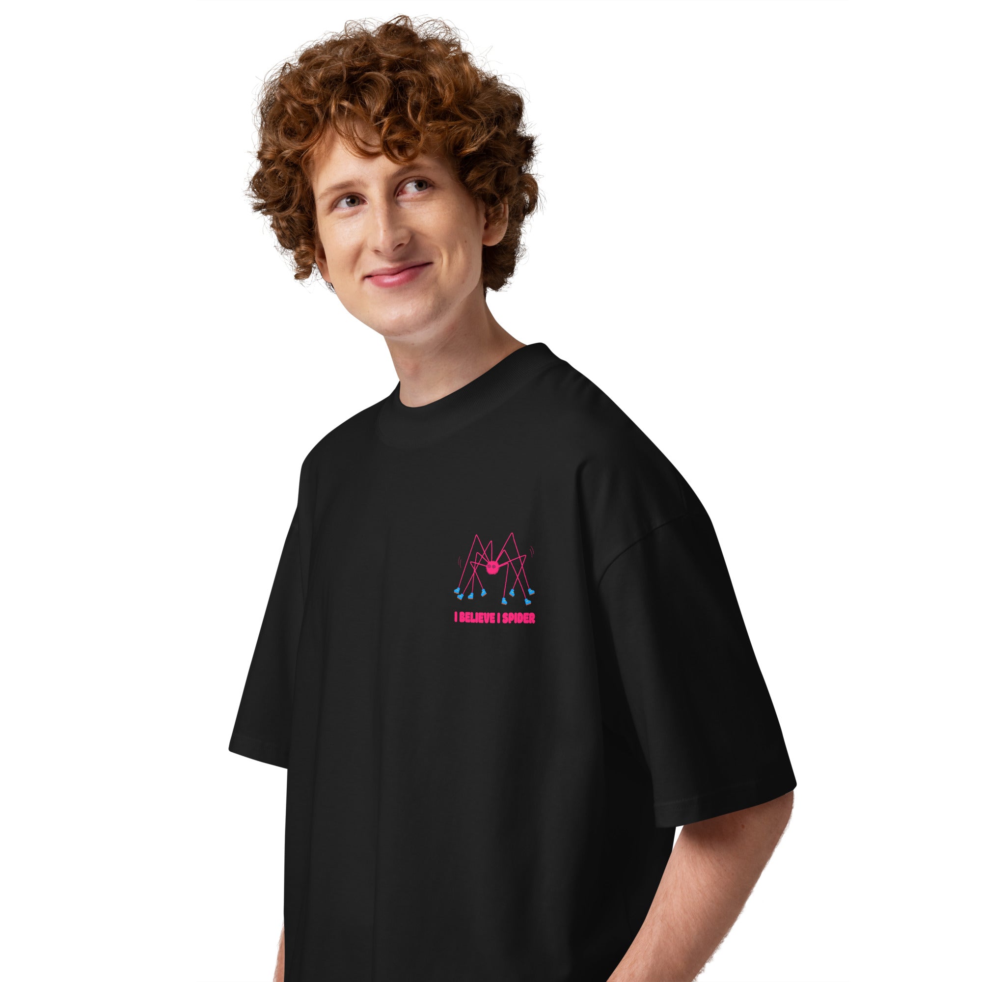 A person wearing a black oversized graphic tshirt with a pink spider wearing roller skates and the text "I believe I spider" printed on the left chest