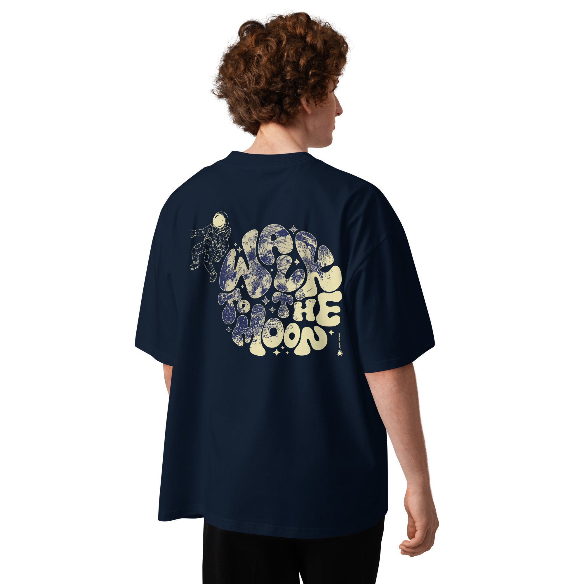A person shown from the back wearing an oversized navy blue T-shirt with a large vintage-style graphic on the back. The graphic features cream and blue abstract shapes and the words 'Moon' and 'The Moon' in a retro font.