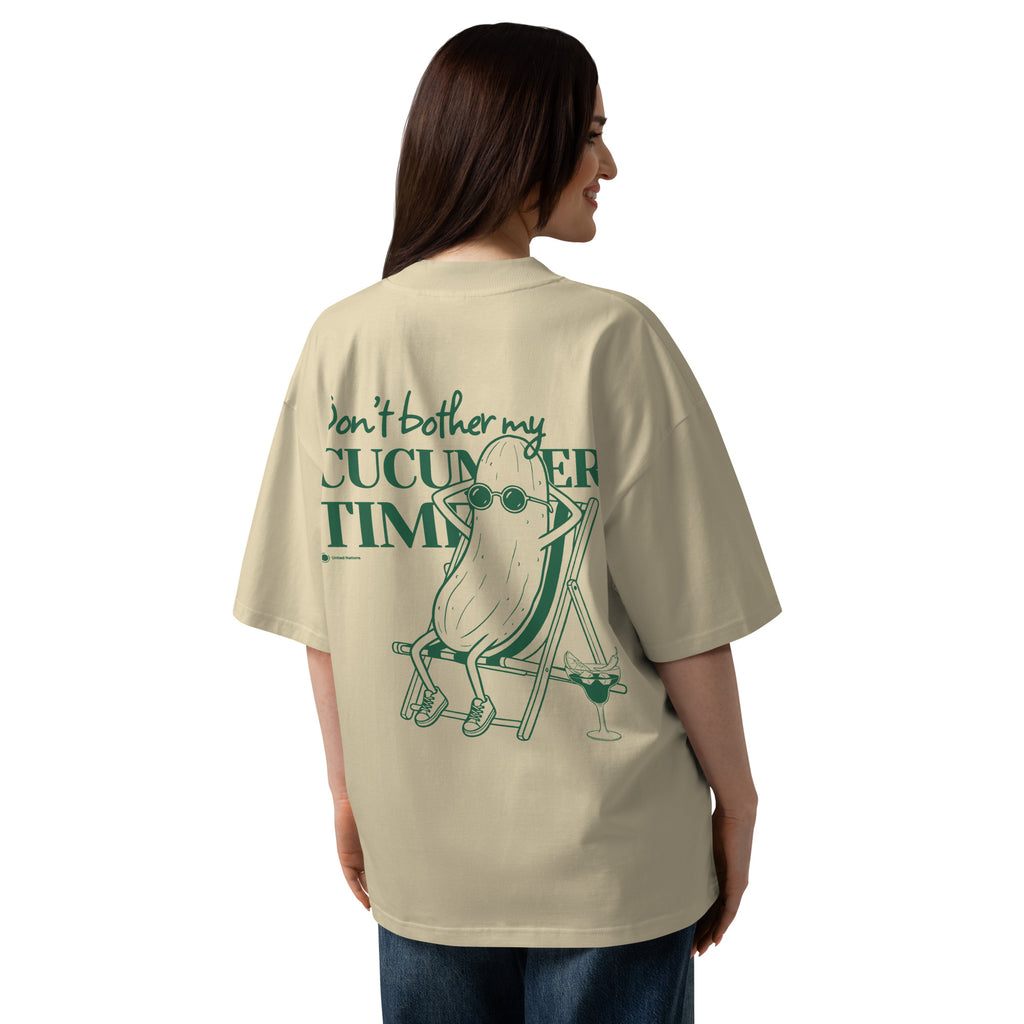 A woman shown from the back wearing an oversized beige graphic T-shirt with a green illustration and text reading 'Don't bother my CUCUMBER TIME.'.