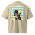 A beige short-sleeve t-shirt shown from the back, featuring a large graphic print of a dachshund wearing blue sunglasses and a yellow bandana against a yellow and blue striped background.