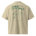 Beige short-sleeve t-shirt shown from the back, featuring a green graphic of a cucumber wearing sunglasses and sitting on an ice cube, with the text 'COOL as a CUCUMBER'.