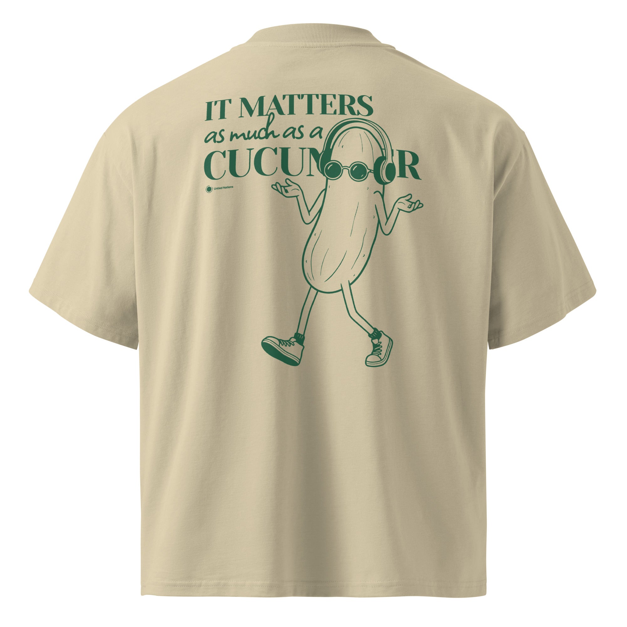 A beige short-sleeve t-shirt shown from the back, featuring a green graphic of a walking cucumber character wearing headphones and the text 'IT MATTERS as much as a CUCUMBER'.
