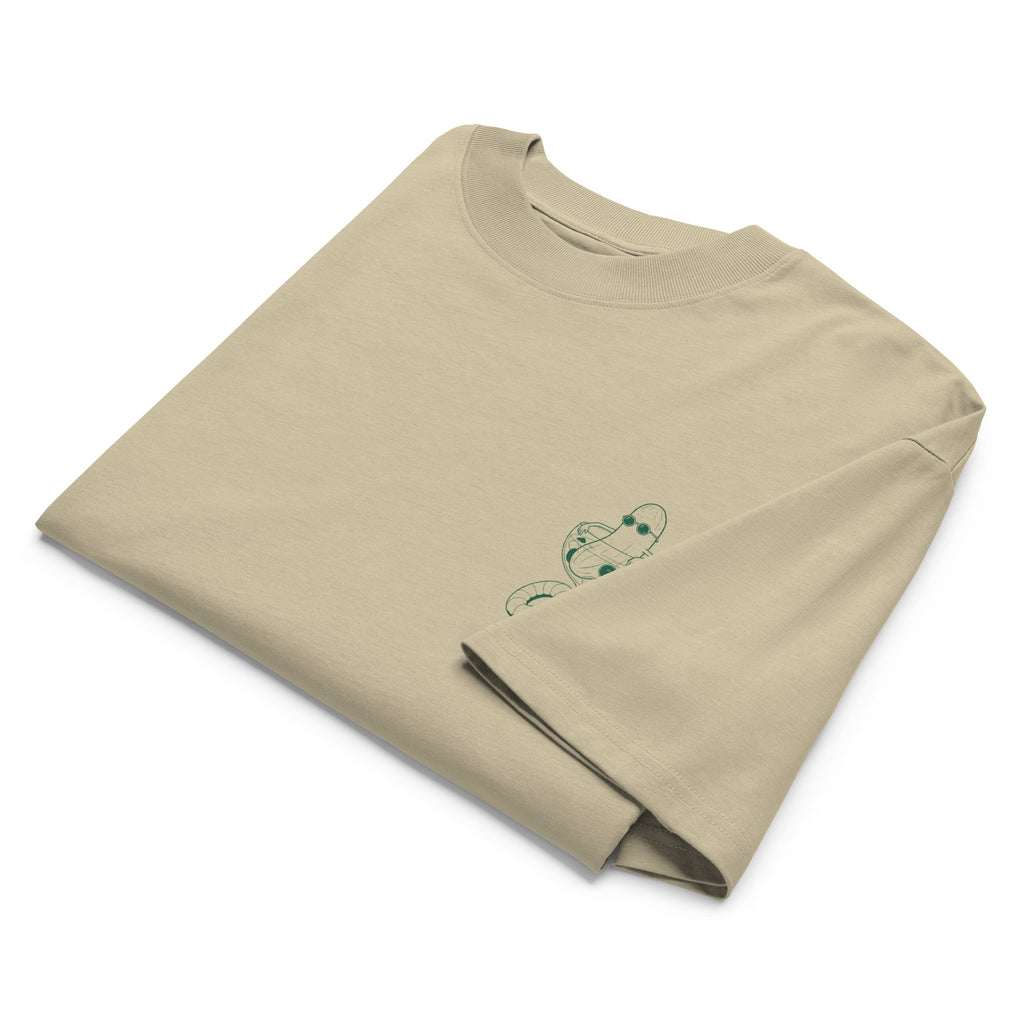 A folded beige short-sleeve crewneck t-shirt with a small green illustration of a cucumber wearing sunglasses and sitting in a cocktail glass printed on the left chest.