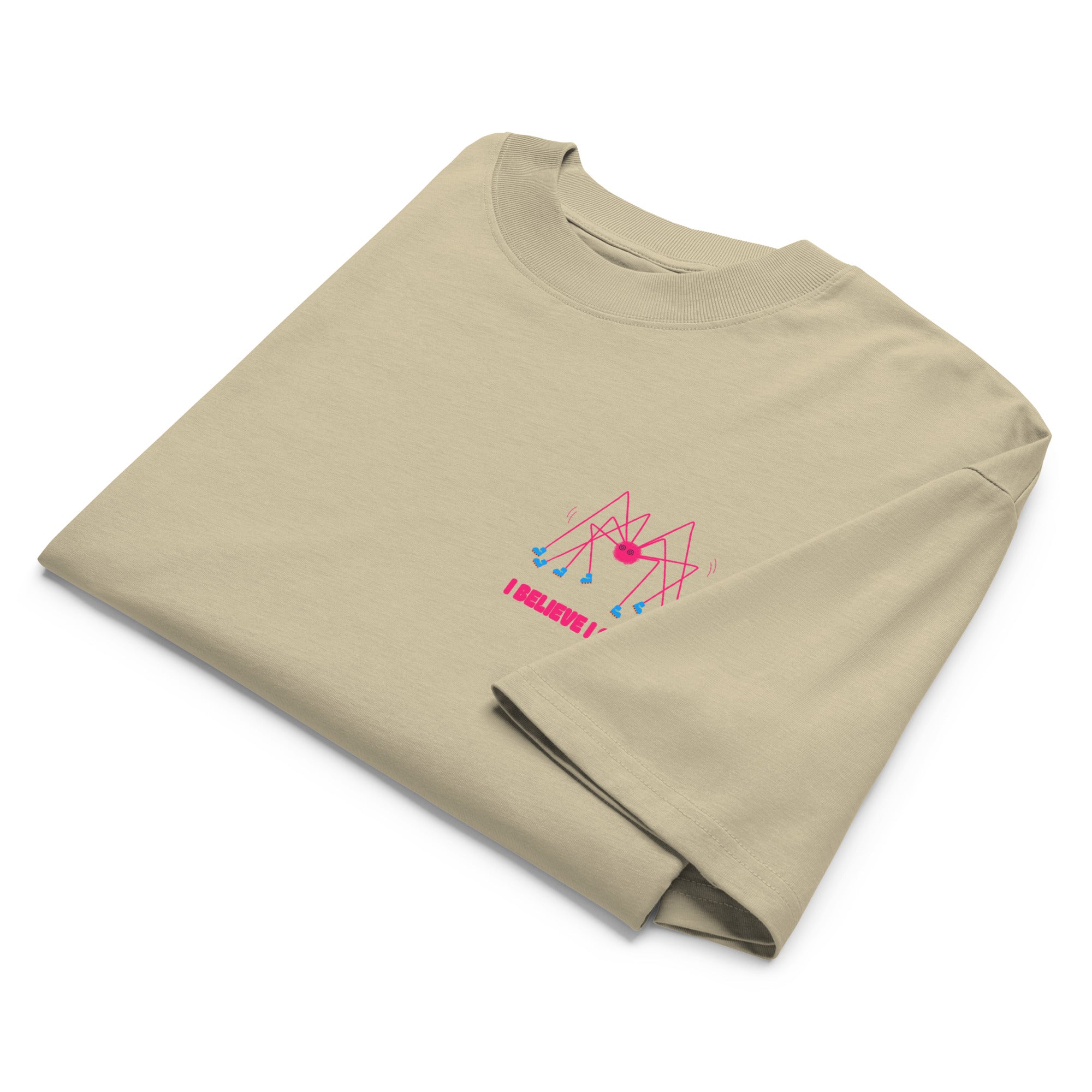 A folded beige oversized graphic tshirt with a pink spider wearing roller skates and the text "I believe I spider" printed on the left chest