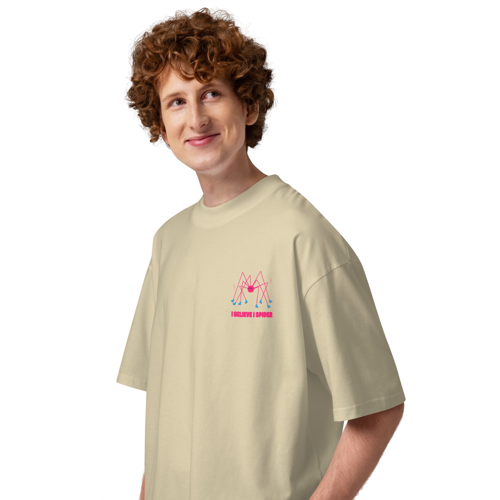 A person wearing a beige oversized graphic tshirt with a pink spider wearing roller skates and the text "I believe I spider" printed on the left chest