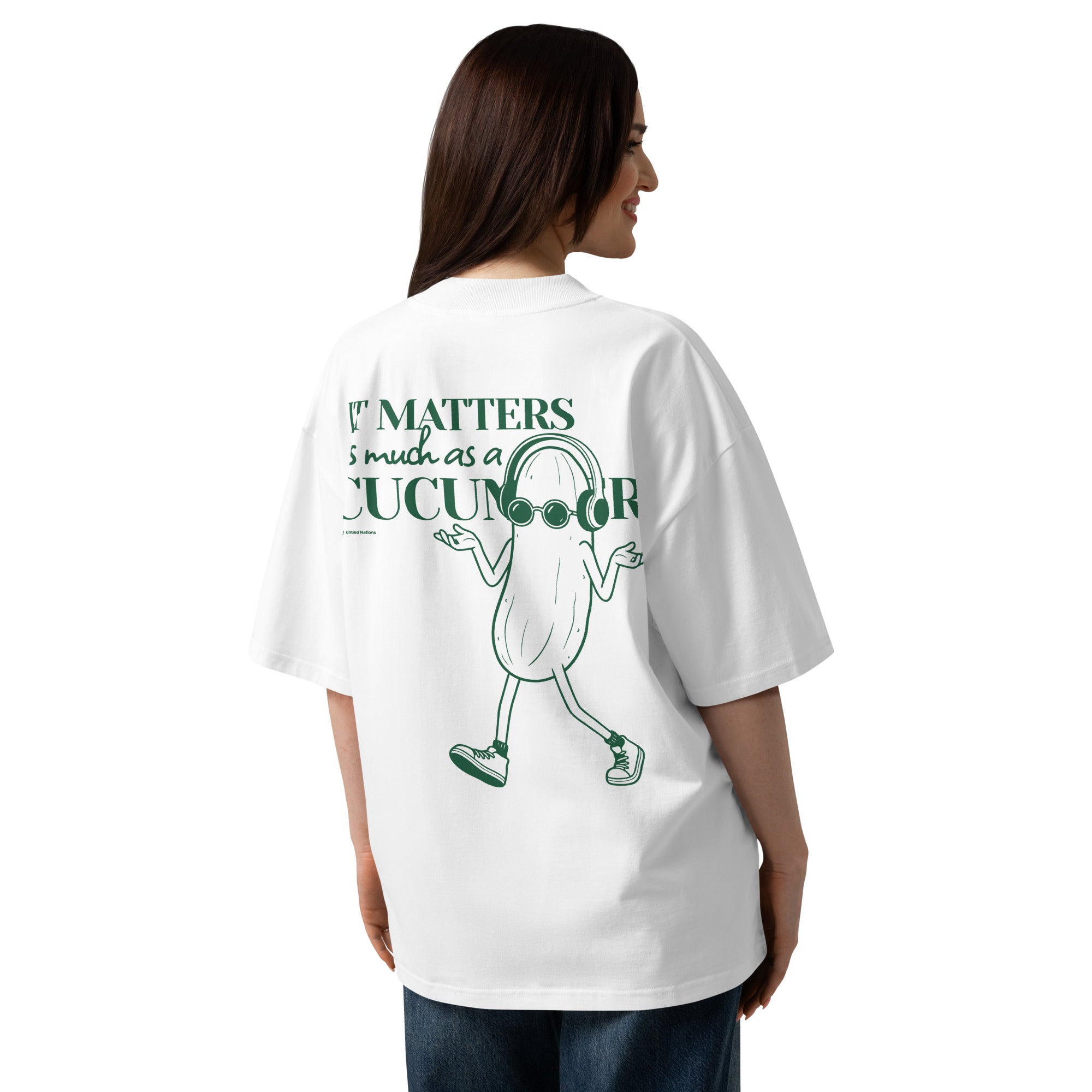 A woman shown from the back wearing an oversized white graphic T-shirt with a green cartoon cucumber character and the text 'It matters as much as a cucumber'.
