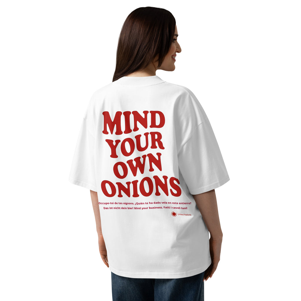 A woman shown from the back wearing an oversized white T-shirt with large red text reading 'MIND YOUR OWN ONIONS' across the back, paired with blue jeans, on a plain white studio background.
