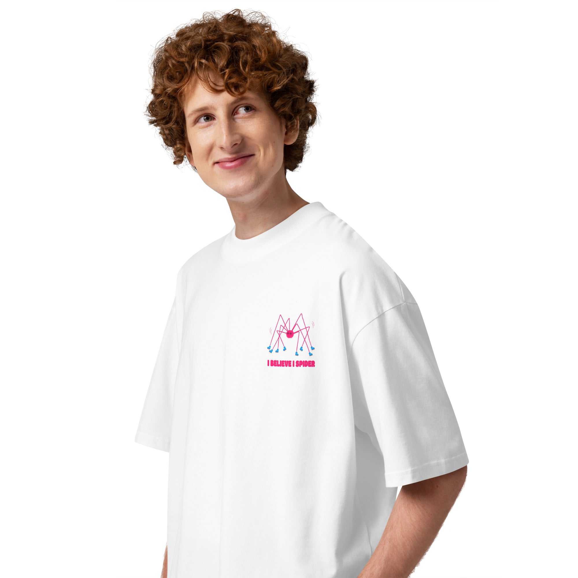 A person wearing a white oversized graphic tshirt with a pink spider wearing roller skates and the text "I believe I spider" printed on the left chest