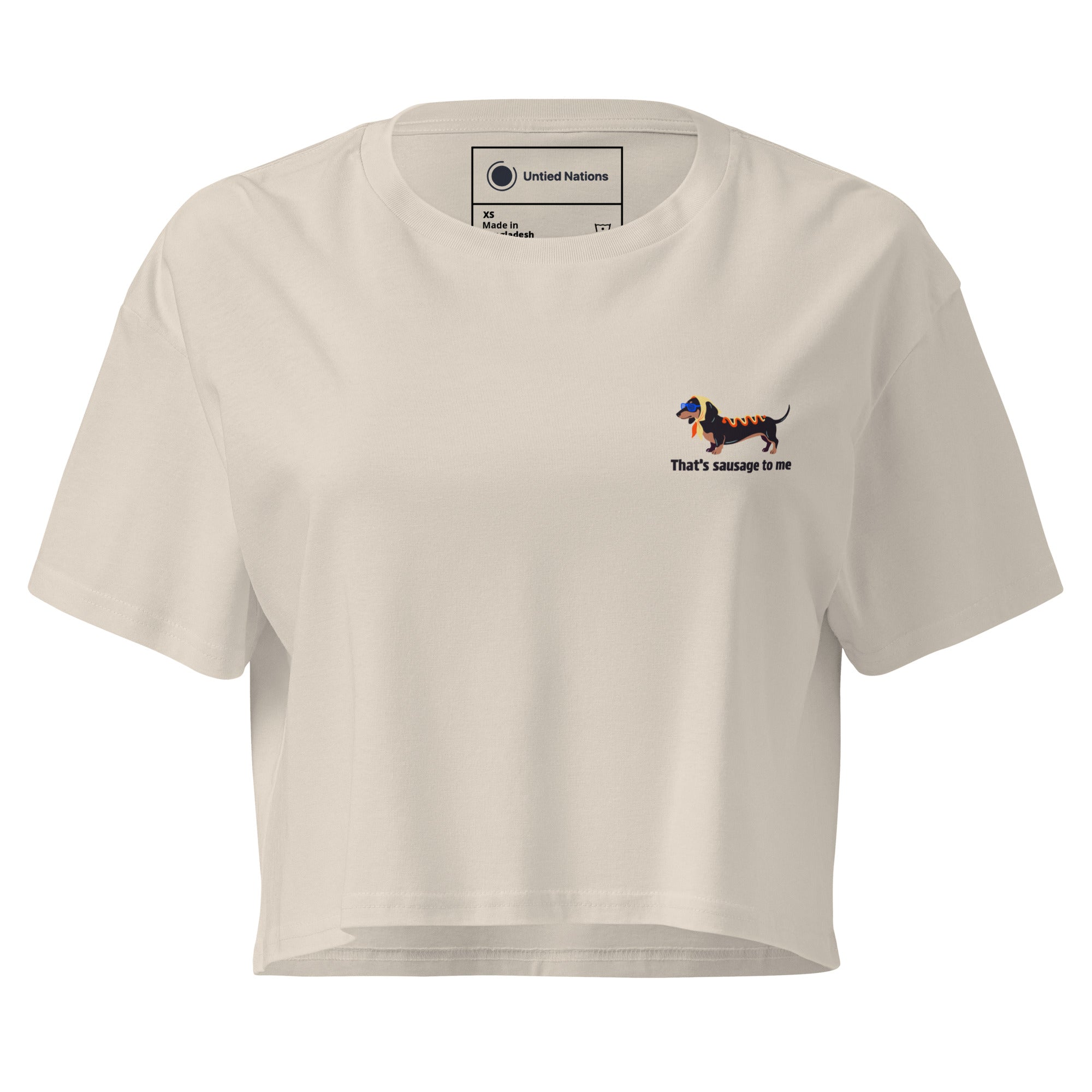 A cream-colored short-sleeve crop top t-shirt with a small graphic of a dachshund on the left chest and the text 'that's sausage to me' underneath, displayed on a clean white background.