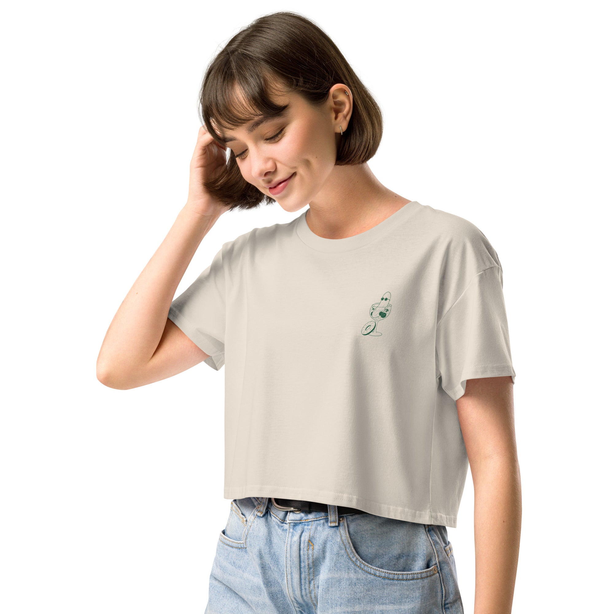 Woman wearing a beige t-shirt with an illustration of a cucumber wearing sunglasses sitting in a cocktail glass printed on the left chest.