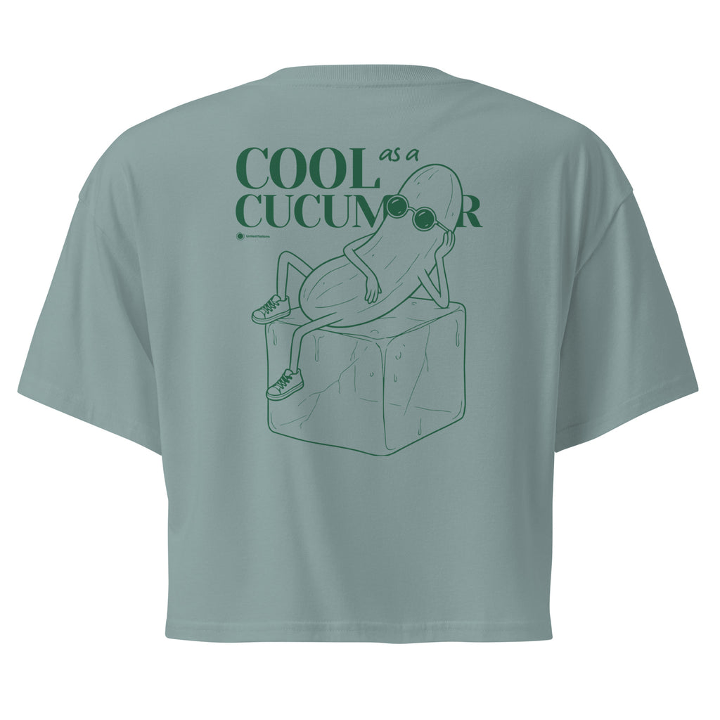 Teal short-sleeve crop top shown from the back, featuring a green line art graphic of a cucumber character wearing sunglasses and sitting on an ice cube, with the text 'COOL as a CUCUMBER'.