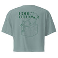 Teal short-sleeve crop top shown from the back, featuring a green line art graphic of a cucumber character wearing sunglasses and sitting on an ice cube, with the text 'COOL as a CUCUMBER'.