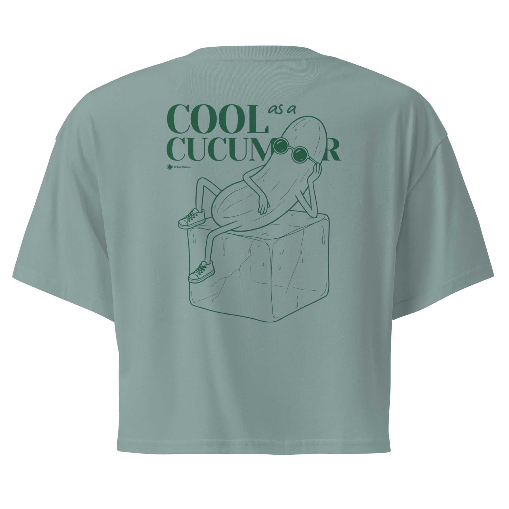 Teal short-sleeve crop top shown from the back, featuring a green line art graphic of a cucumber character wearing sunglasses and sitting on an ice cube, with the text 'COOL as a CUCUMBER'.