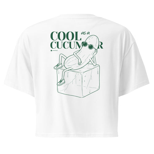 White short-sleeve crop top shown from the back, featuring a green line art graphic of a cucumber character wearing sunglasses and sitting on an ice cube, with the text 'COOL as a CUCUMBER'.