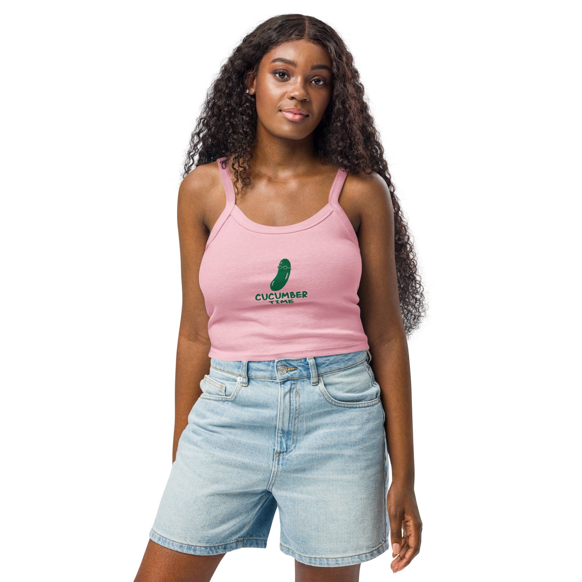 Woman wearing a pink tank top with a green design and light blue denim shorts on a white background